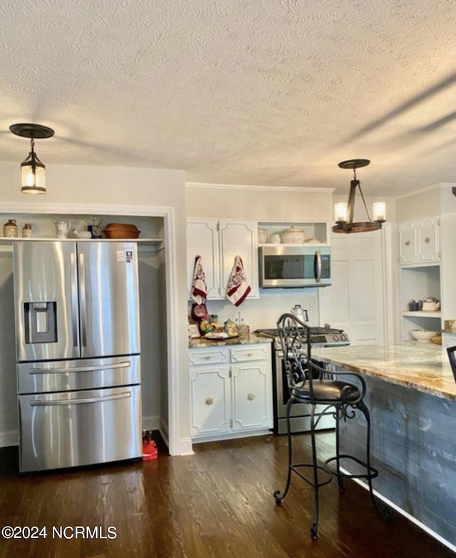 kitchen with appliances with stainless steel finishes, dark wood finished floors, a textured ceiling, white cabinets, and pendant lighting