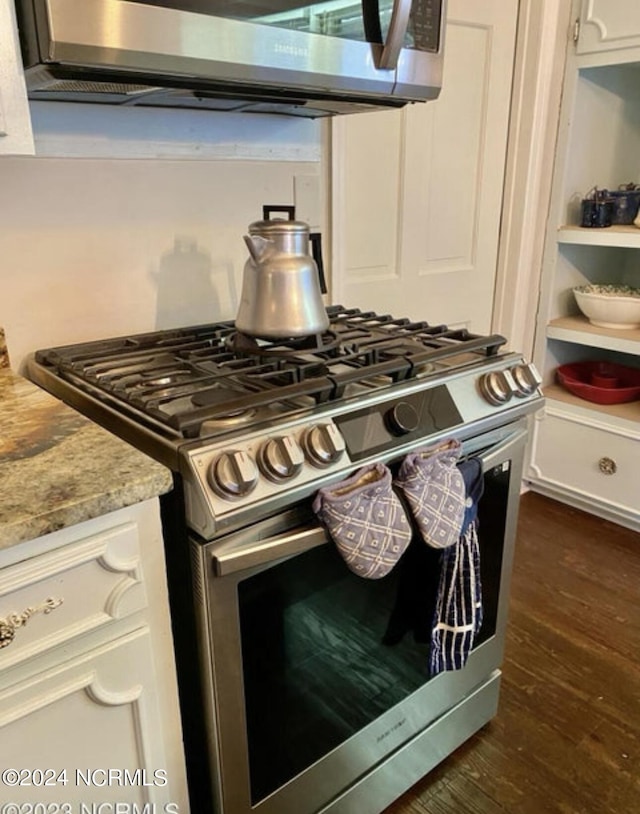 kitchen view of stainless steel appliances, dark wood finished floors, white cabinets, and extractor fan