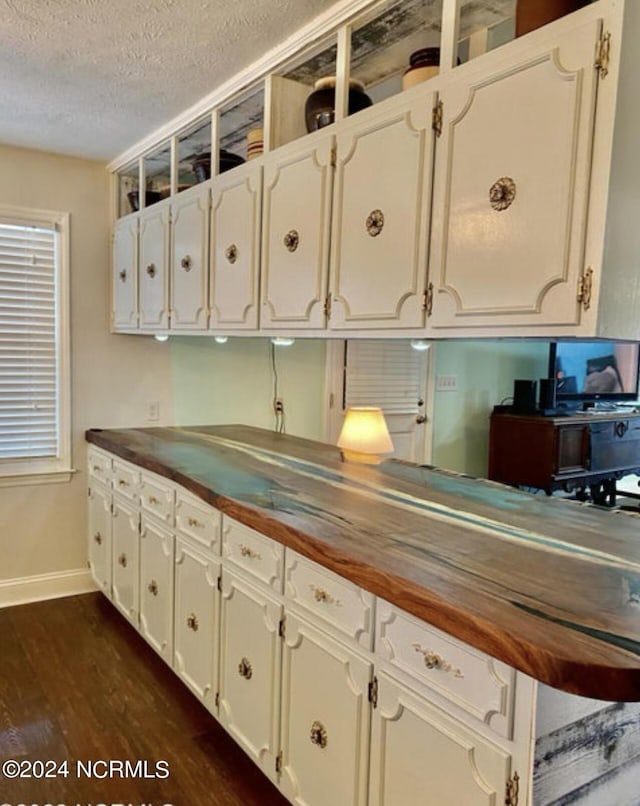 kitchen with butcher block counters, dark wood-type flooring, white cabinets, a textured ceiling, and baseboards