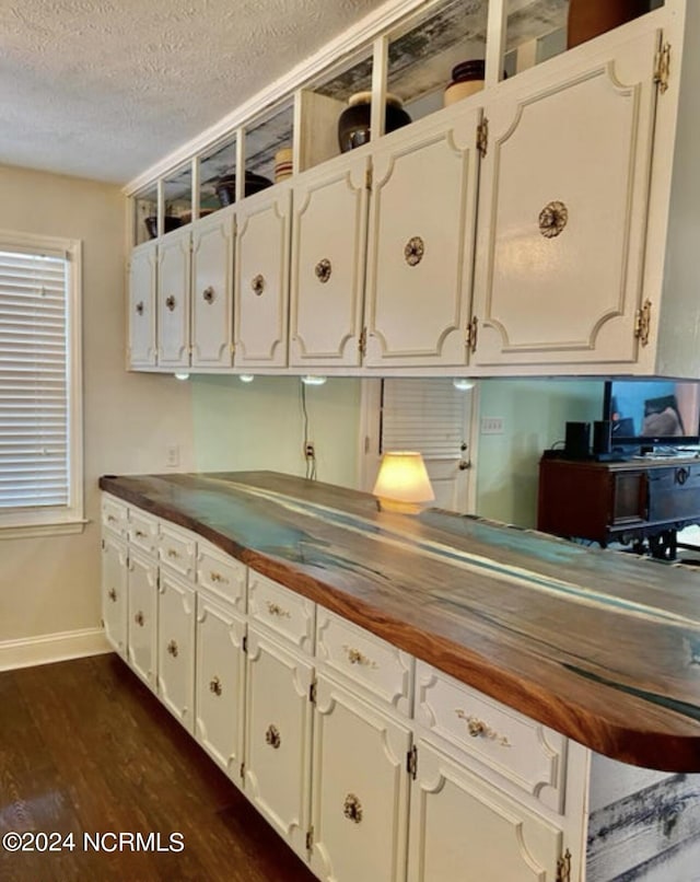 kitchen with wooden counters, baseboards, dark wood-style flooring, a textured ceiling, and white cabinets