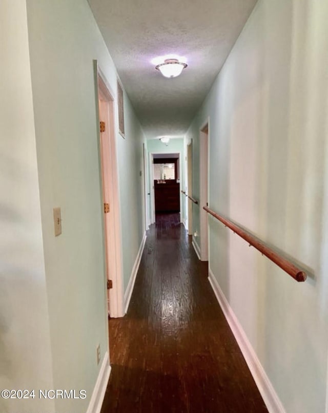 hall featuring a textured ceiling, baseboards, and hardwood / wood-style floors