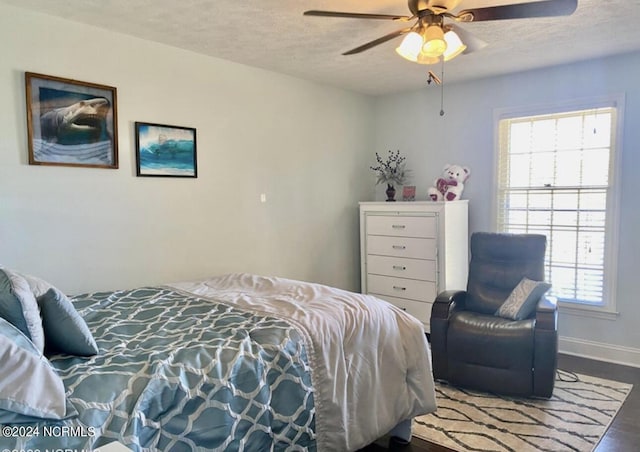 bedroom featuring a ceiling fan, a textured ceiling, baseboards, and wood finished floors