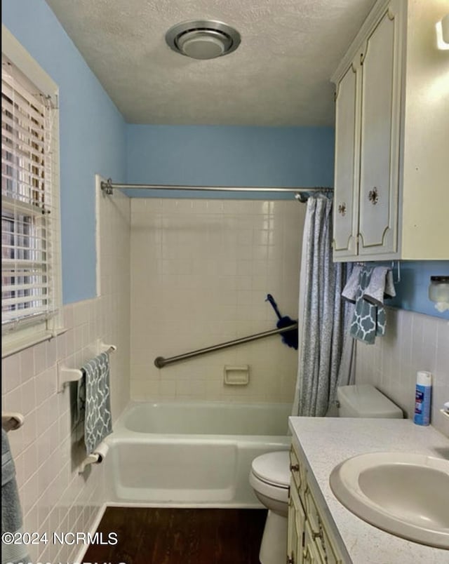 bathroom featuring a wainscoted wall, tile walls, shower / bath combination with curtain, toilet, and a textured ceiling