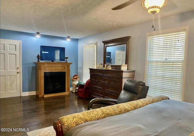 bedroom featuring wood finished floors, a textured ceiling, a fireplace, baseboards, and ceiling fan