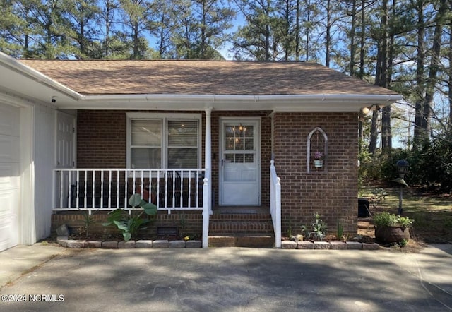 entrance to property featuring a garage, covered porch, brick siding, and concrete driveway