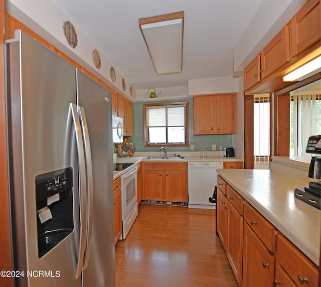 kitchen with light countertops, white appliances, a sink, and light wood-style floors