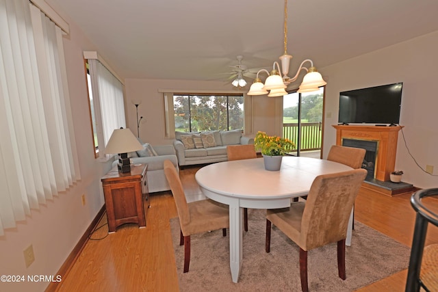 dining area featuring a chandelier, baseboards, a fireplace with raised hearth, and light wood finished floors