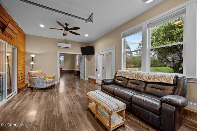 living room featuring an AC wall unit, a healthy amount of sunlight, baseboards, and wood finished floors