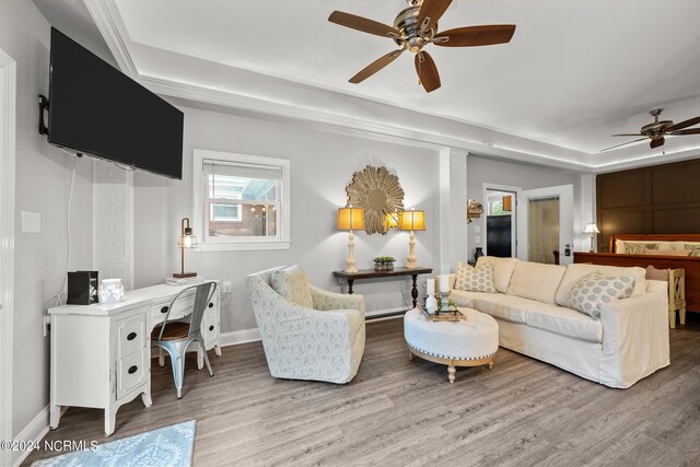 living room with a tray ceiling, wood finished floors, a ceiling fan, and baseboards