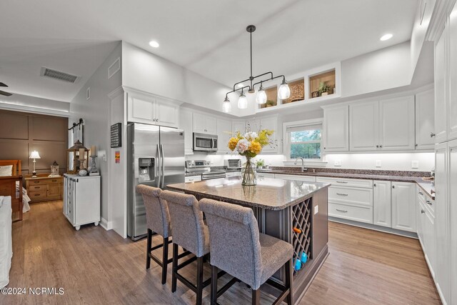 kitchen with light hardwood / wood-style flooring, white cabinets, pendant lighting, stainless steel appliances, and a kitchen island