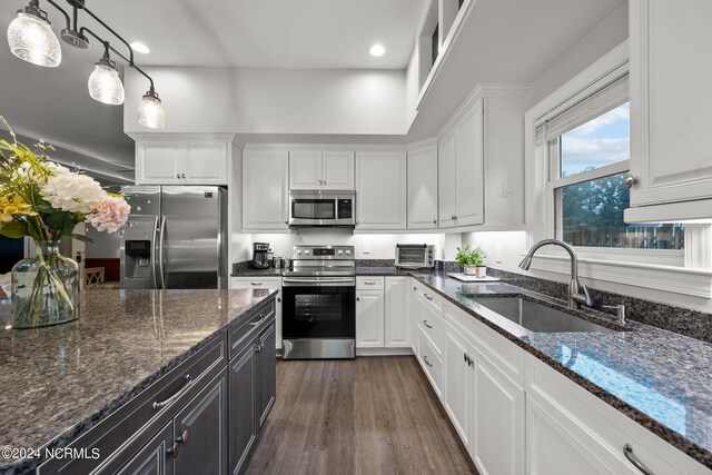 kitchen with dark stone counters, white cabinets, appliances with stainless steel finishes, pendant lighting, and a sink