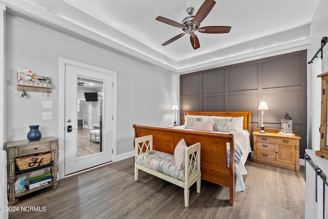 bedroom featuring a barn door, a ceiling fan, a decorative wall, and wood finished floors