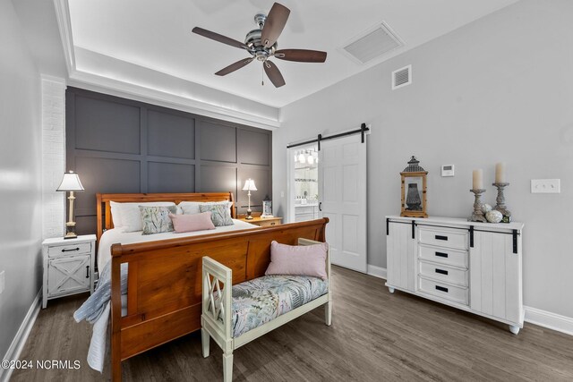 bedroom with a barn door, dark hardwood / wood-style flooring, and ceiling fan