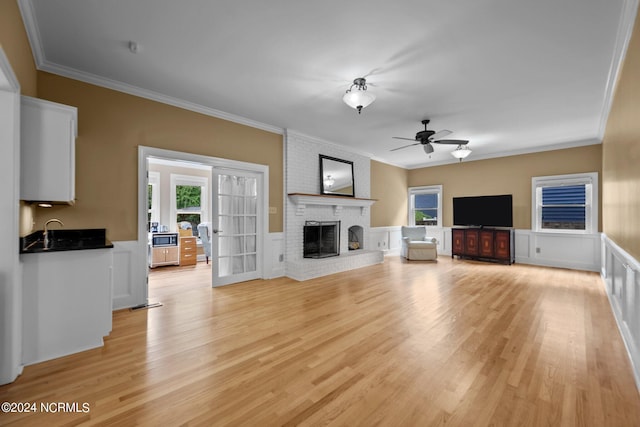 unfurnished living room featuring light wood-type flooring, a fireplace, crown molding, ceiling fan, and brick wall