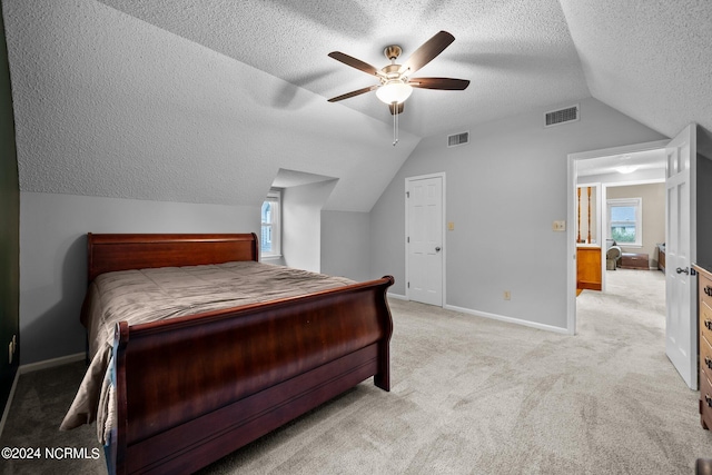 bedroom with ceiling fan, a textured ceiling, light carpet, and vaulted ceiling