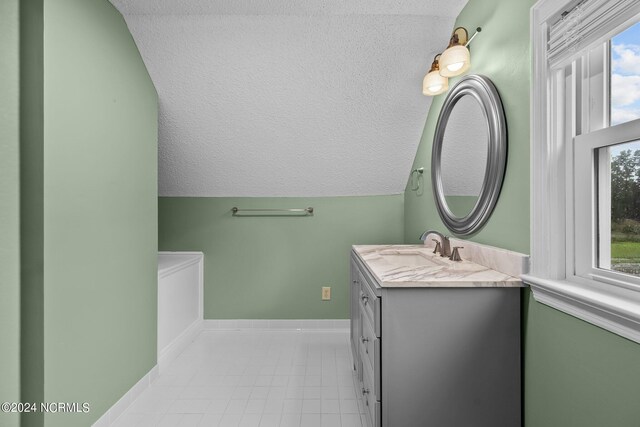 bathroom with a textured ceiling, vanity, vaulted ceiling, and tile patterned flooring