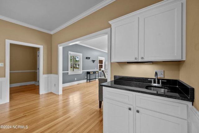 kitchen with ornamental molding, white cabinets, a sink, dark stone countertops, and light wood-type flooring