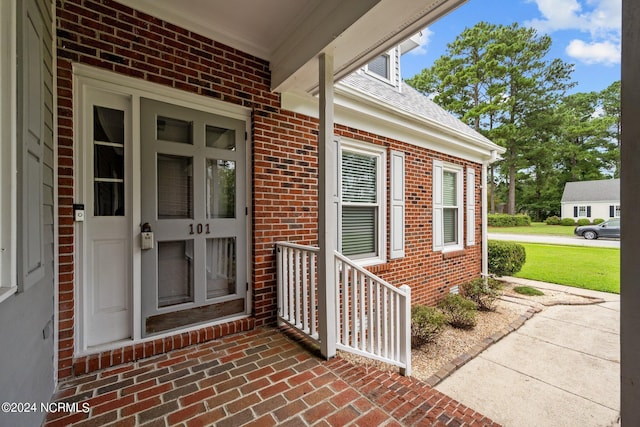 property entrance with a shingled roof and brick siding