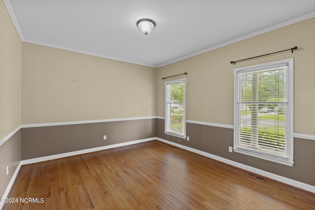 empty room featuring hardwood / wood-style floors, crown molding, and a wealth of natural light