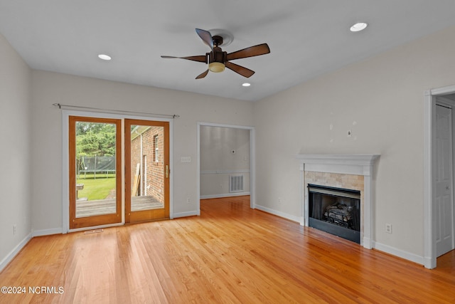 unfurnished living room featuring a tile fireplace, ceiling fan, and light hardwood / wood-style floors