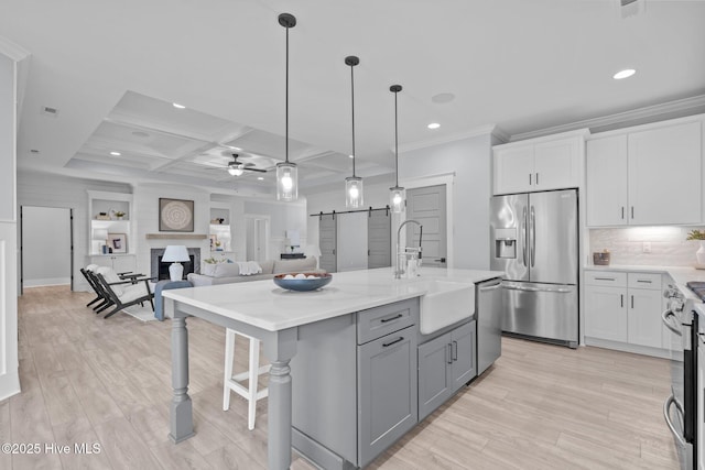 kitchen with a fireplace, stainless steel appliances, gray cabinets, a barn door, and ceiling fan