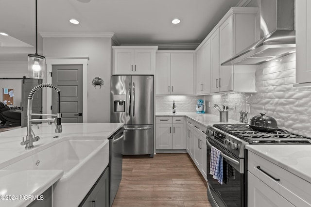 kitchen with stainless steel appliances, crown molding, wall chimney range hood, white cabinetry, and a sink