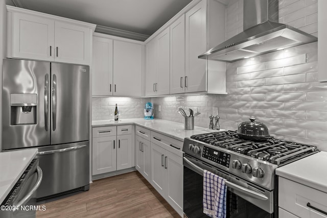 kitchen featuring wall chimney range hood, appliances with stainless steel finishes, light countertops, and decorative backsplash