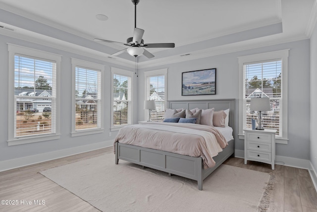 bedroom with light wood-style floors, a tray ceiling, multiple windows, and ornamental molding