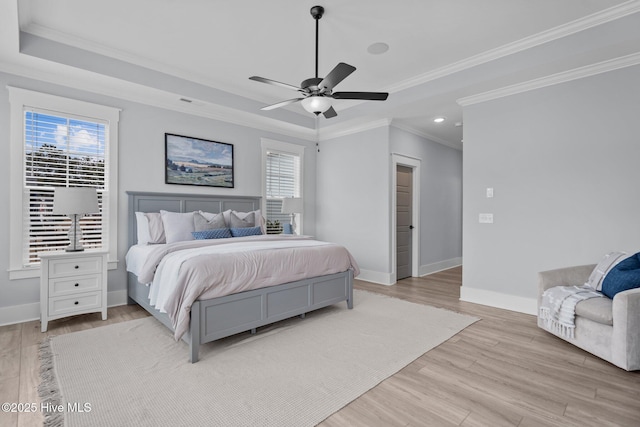 bedroom with light wood finished floors, a tray ceiling, multiple windows, and baseboards