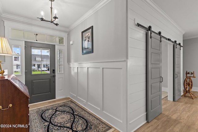 entrance foyer featuring a chandelier, a barn door, light wood-style flooring, a decorative wall, and ornamental molding