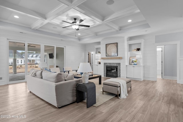 living area with light wood-type flooring, a glass covered fireplace, beam ceiling, and coffered ceiling