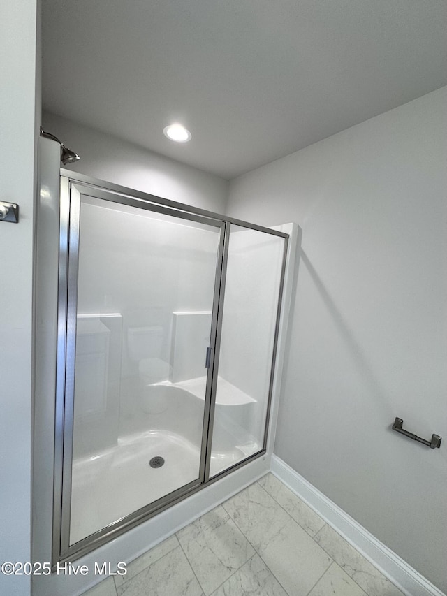 bathroom with marble finish floor, a shower stall, and baseboards