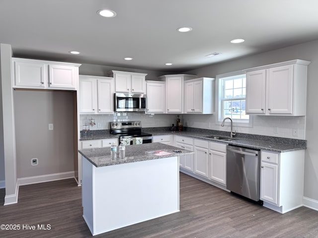 kitchen featuring visible vents, a kitchen island, stainless steel appliances, white cabinetry, and a sink