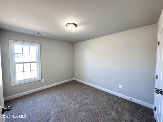 spare room featuring visible vents, dark carpet, and baseboards