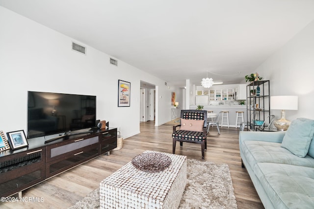 living room with light wood-style floors, a chandelier, visible vents, and baseboards