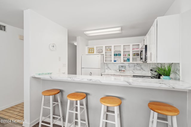 kitchen with stainless steel appliances, tasteful backsplash, a peninsula, and light stone counters