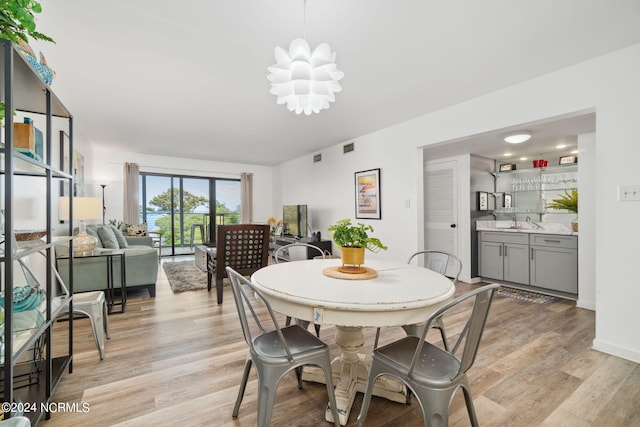 dining area with light wood-style flooring, a notable chandelier, visible vents, baseboards, and wet bar