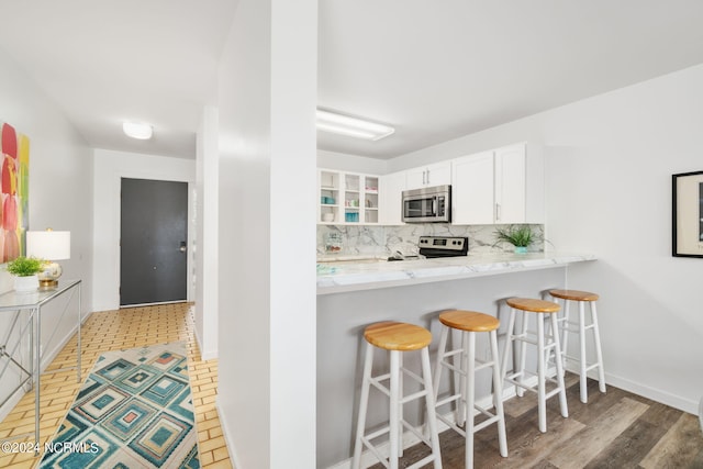 kitchen featuring baseboards, white cabinets, decorative backsplash, appliances with stainless steel finishes, and a breakfast bar