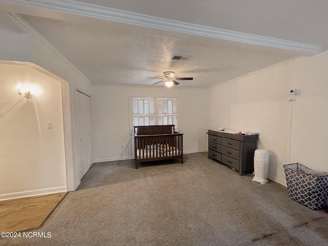 carpeted bedroom featuring ceiling fan, crown molding, and a nursery area