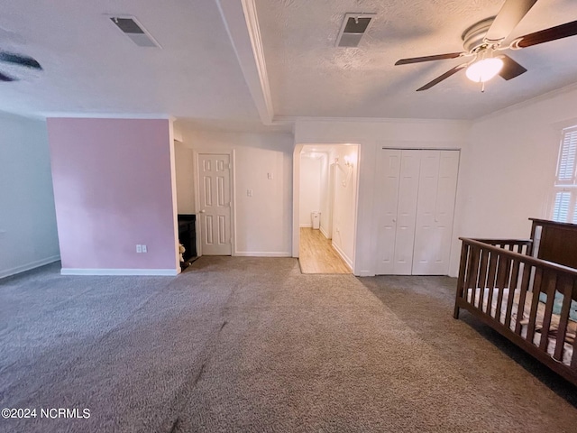 unfurnished bedroom with ceiling fan, a nursery area, ornamental molding, a closet, and carpet flooring