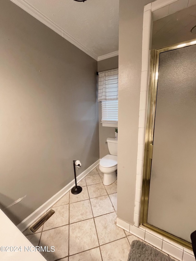 bathroom with tile patterned flooring, toilet, crown molding, and a shower with shower door