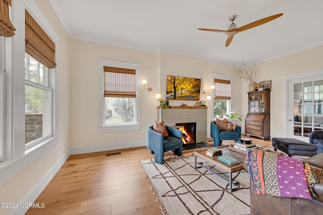 living room featuring crown molding, a healthy amount of sunlight, a fireplace, and light hardwood / wood-style flooring