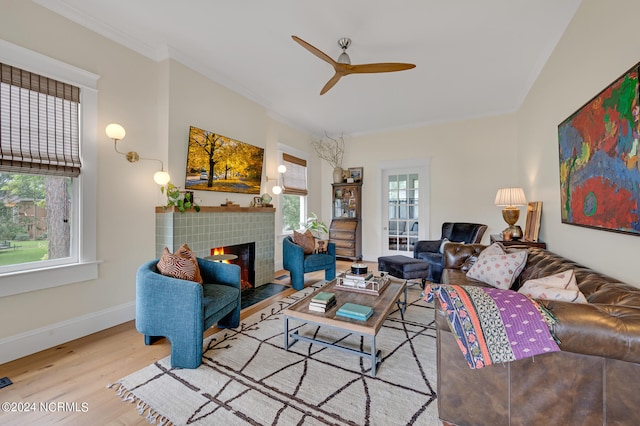 living room with a tiled fireplace, ornamental molding, ceiling fan, and light wood-type flooring