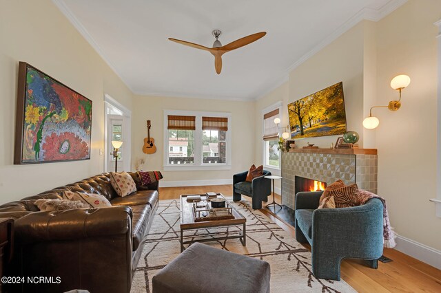 living room with ornamental molding, light hardwood / wood-style floors, a tile fireplace, and ceiling fan