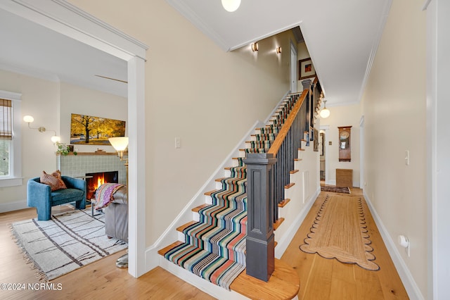 staircase with a tile fireplace, crown molding, and hardwood / wood-style floors