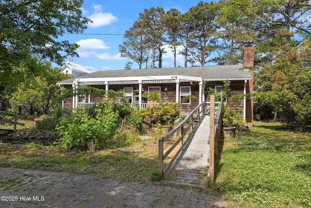 view of front of home featuring a front lawn, covered porch, roof with shingles, and a chimney
