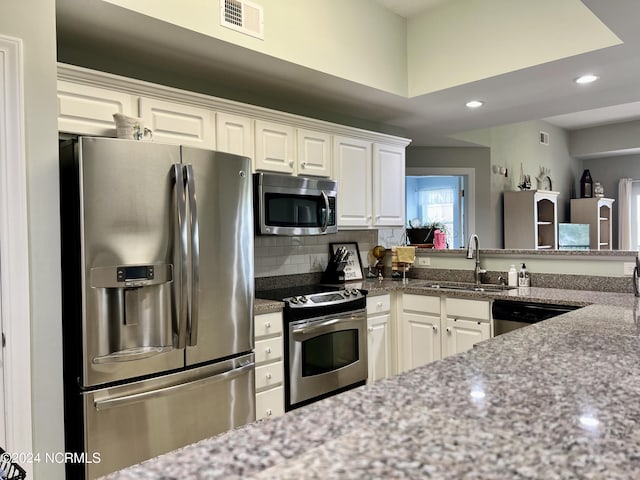 kitchen featuring sink, white cabinetry, dark stone countertops, stainless steel appliances, and decorative backsplash