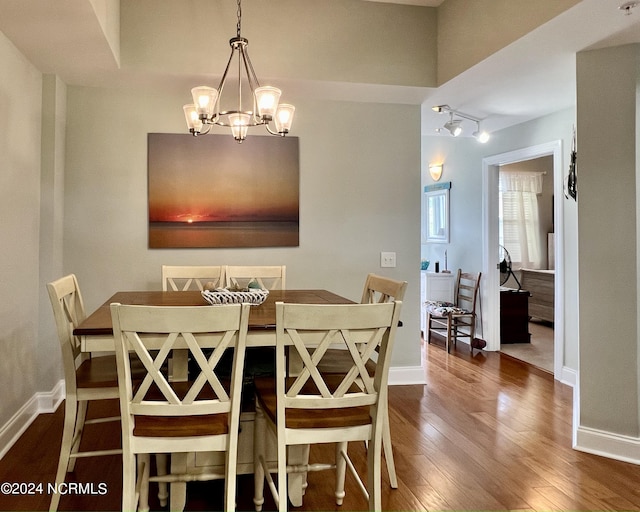 dining space with rail lighting, dark wood-type flooring, and a notable chandelier