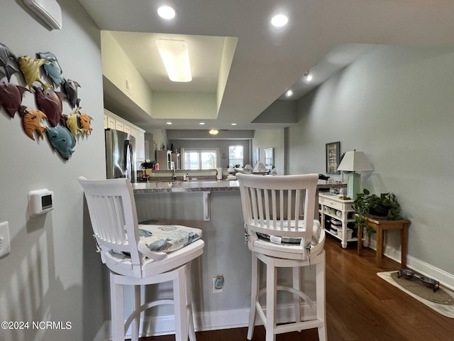 kitchen featuring stainless steel fridge, kitchen peninsula, white cabinets, a kitchen bar, and a raised ceiling