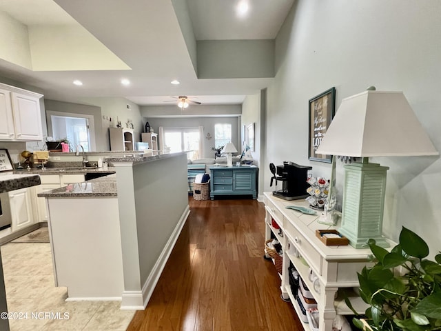 kitchen with stone counters, white cabinetry, a center island, ceiling fan, and dark wood-type flooring